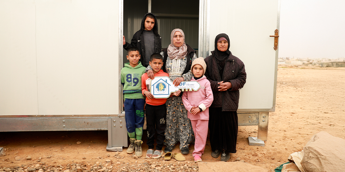 A family of seven standing at the door of their new HDF caravan home in Jordan